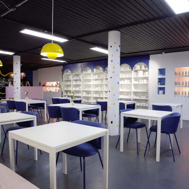 Moderne Café-Umgebung mit weißen Tischen, blauen Stühlen und regalen im Hintergrund.